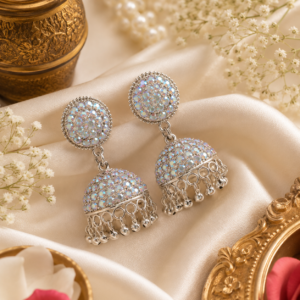 Silver crystal jhumka earrings with rhinestone detailing and dangling silver bead charms by Shining Riva displayed on ivory satin fabric.